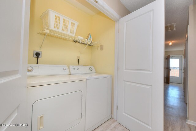 clothes washing area featuring a textured ceiling, electric dryer hookup, independent washer and dryer, and light hardwood / wood-style floors