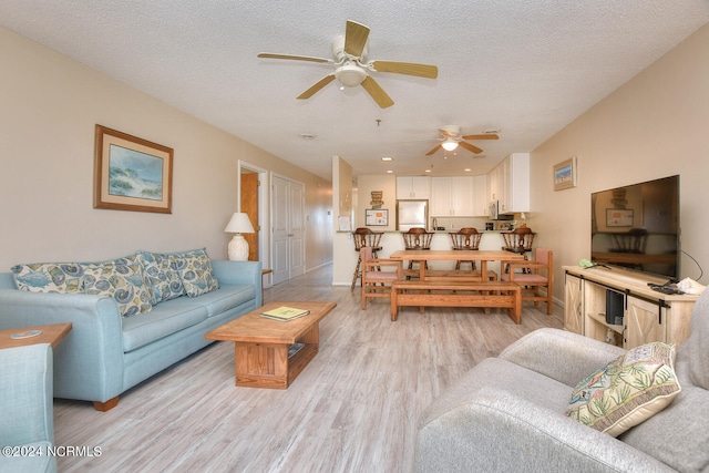 living room with a textured ceiling, light hardwood / wood-style floors, and ceiling fan