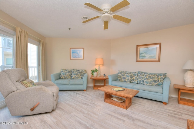 living room featuring light hardwood / wood-style flooring, ceiling fan, and a textured ceiling