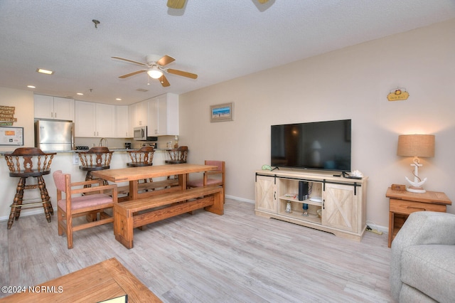 living room featuring a textured ceiling, ceiling fan, and light wood-type flooring