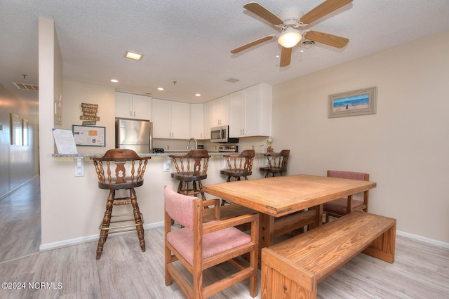 dining area featuring light hardwood / wood-style flooring, ceiling fan, and a textured ceiling