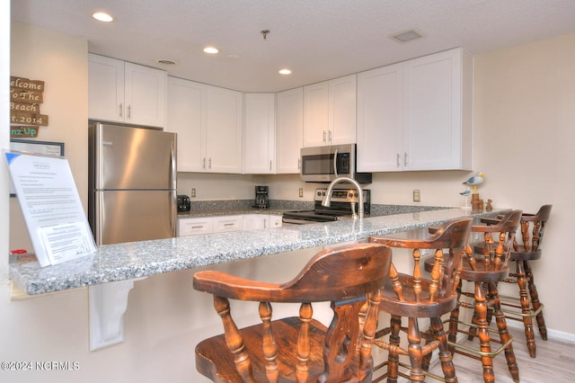 kitchen with a breakfast bar area, kitchen peninsula, appliances with stainless steel finishes, and light stone counters