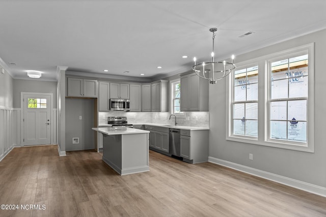 kitchen with stainless steel appliances, light wood-type flooring, gray cabinets, a kitchen island, and backsplash