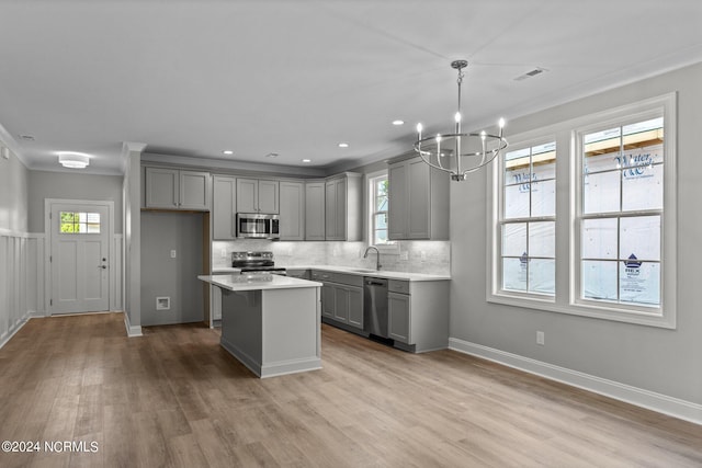 kitchen with appliances with stainless steel finishes, gray cabinets, a kitchen island, pendant lighting, and decorative backsplash