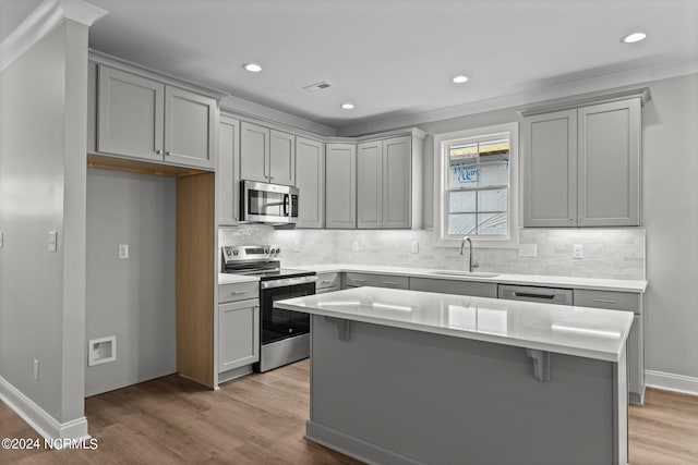 kitchen with light wood-type flooring, a kitchen island, appliances with stainless steel finishes, sink, and tasteful backsplash