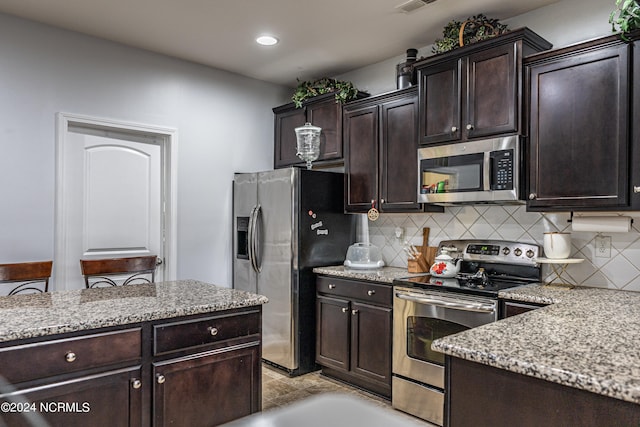 kitchen with light stone countertops, decorative backsplash, appliances with stainless steel finishes, and dark brown cabinetry