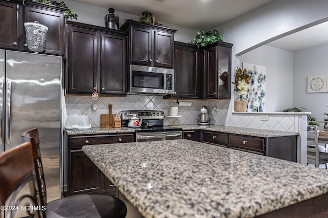 kitchen with decorative backsplash, stainless steel appliances, light stone counters, and dark brown cabinetry