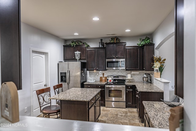 kitchen with tasteful backsplash, a kitchen island, dark brown cabinets, appliances with stainless steel finishes, and a kitchen breakfast bar