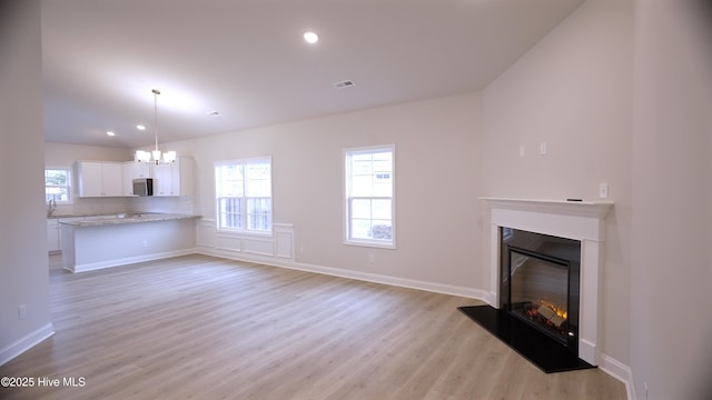 1254 Opaca Dr SE, Bolivia, NC 28422 - unfurnished living room with a chandelier, a glass covered fireplace, light wood-type flooring, baseboards, and recessed lighting
