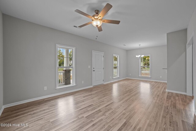 unfurnished living room with light wood-type flooring, a wealth of natural light, and ceiling fan with notable chandelier