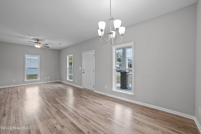 unfurnished room featuring a wealth of natural light, ceiling fan with notable chandelier, and light hardwood / wood-style floors