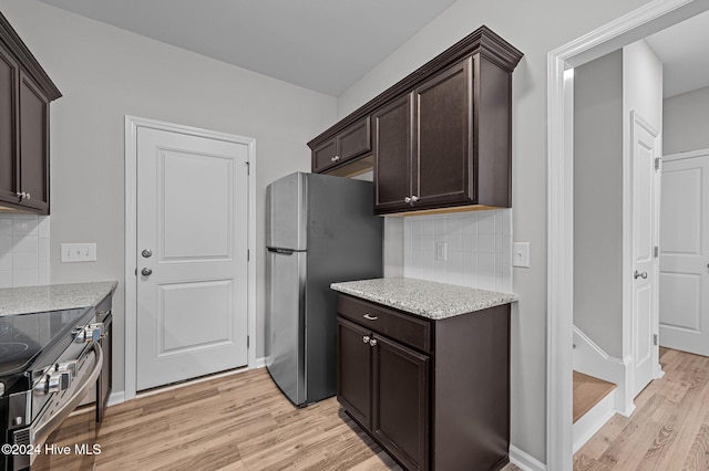 kitchen featuring tasteful backsplash, appliances with stainless steel finishes, dark brown cabinets, light stone countertops, and light hardwood / wood-style flooring