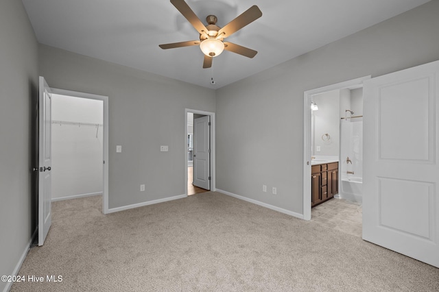 unfurnished bedroom featuring a closet, a spacious closet, ensuite bath, light carpet, and ceiling fan