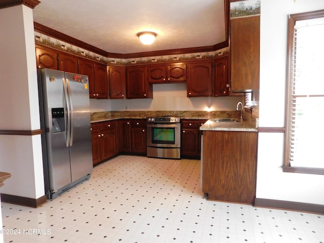 kitchen featuring a healthy amount of sunlight, stainless steel appliances, light stone countertops, sink, and light tile flooring