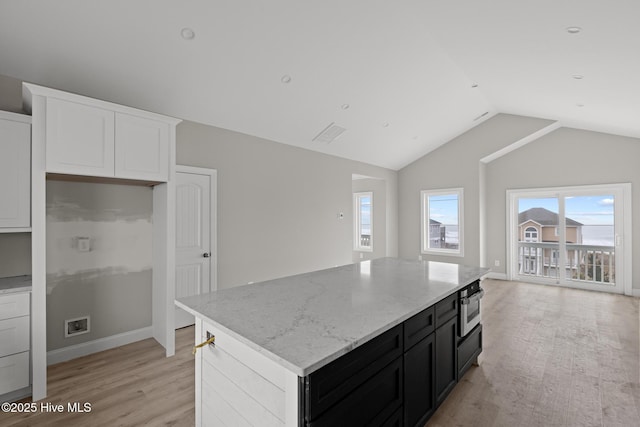 kitchen featuring white cabinets, a center island, light stone countertops, dark cabinetry, and stainless steel oven