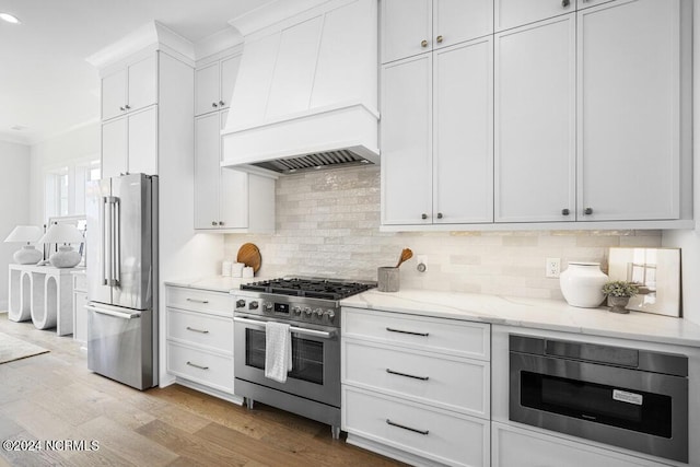 kitchen with white cabinets, stainless steel appliances, decorative backsplash, light wood-type flooring, and custom range hood