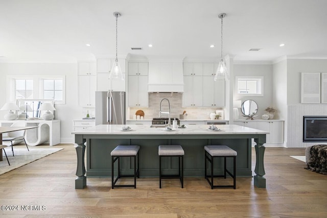 kitchen with white cabinets, custom exhaust hood, a kitchen island with sink, and stainless steel refrigerator