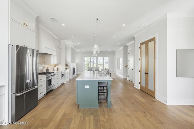 kitchen featuring white cabinets, an island with sink, high end appliances, a kitchen breakfast bar, and hanging light fixtures