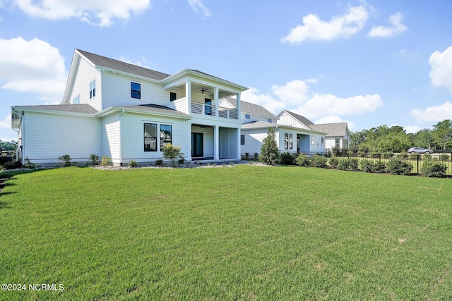 view of front facade with ceiling fan, a balcony, and a front lawn