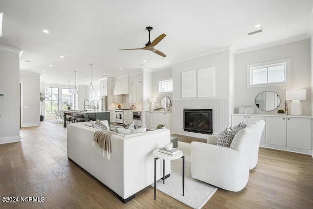 living room with light hardwood / wood-style floors, sink, crown molding, and ceiling fan