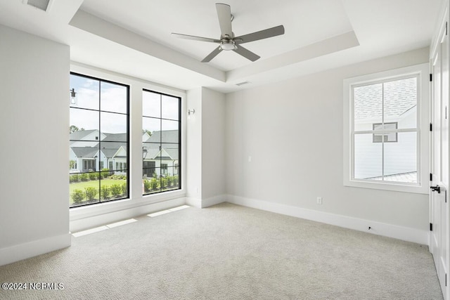 carpeted spare room with ceiling fan, a raised ceiling, and a healthy amount of sunlight