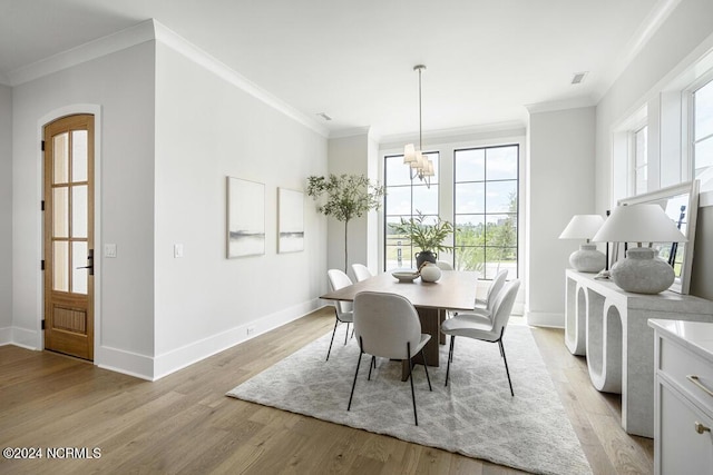 dining space with light hardwood / wood-style floors, ornamental molding, and an inviting chandelier