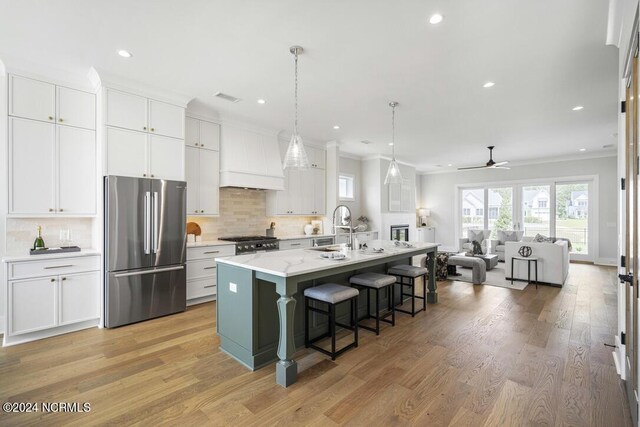 kitchen with a kitchen breakfast bar, light hardwood / wood-style flooring, stainless steel fridge, white cabinets, and an island with sink