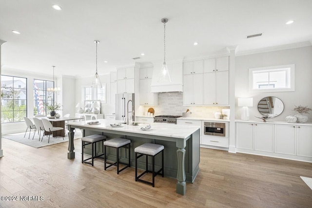 kitchen with stainless steel microwave, white cabinetry, stove, light wood-type flooring, and an island with sink