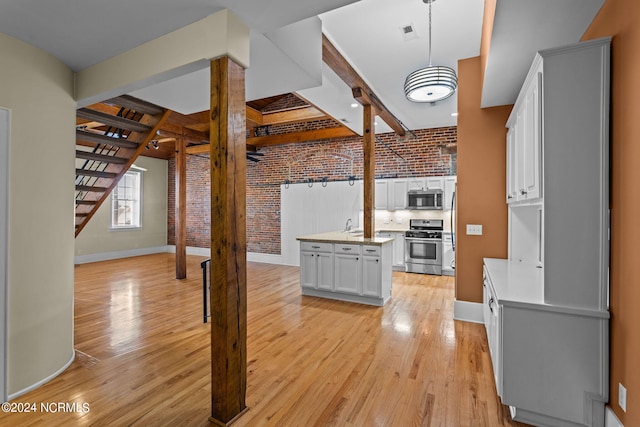 kitchen with brick wall, stainless steel appliances, beamed ceiling, white cabinets, and hanging light fixtures