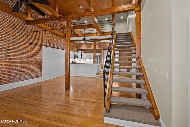 stairs featuring beam ceiling, hardwood / wood-style flooring, ceiling fan, and brick wall