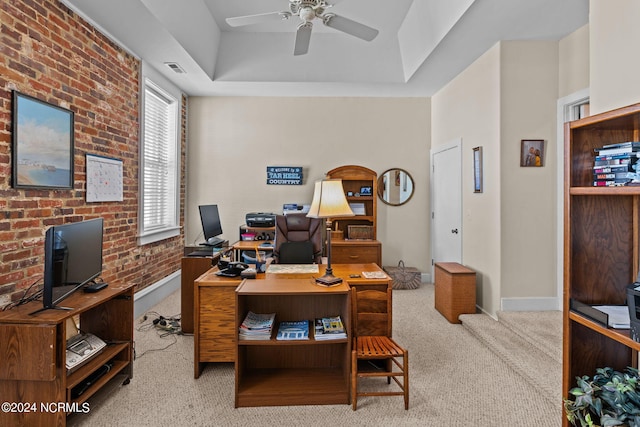 carpeted office featuring a tray ceiling, ceiling fan, and brick wall