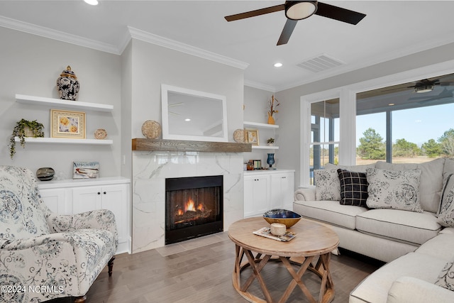 living room featuring built in features, ceiling fan, light hardwood / wood-style floors, crown molding, and a fireplace