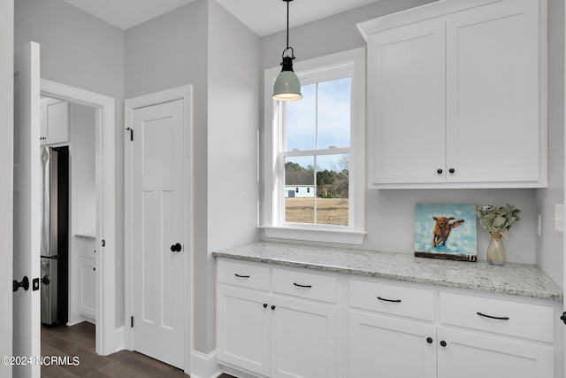 kitchen featuring white cabinetry, dark wood-type flooring, hanging light fixtures, stainless steel fridge with ice dispenser, and light stone countertops