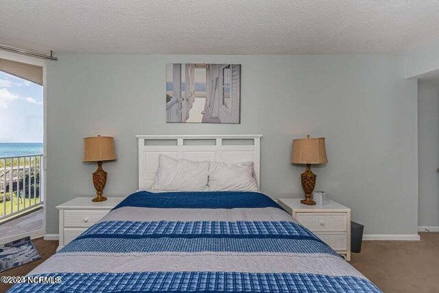 bedroom featuring a water view, a textured ceiling, and light colored carpet