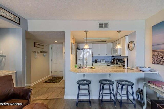 kitchen with kitchen peninsula, decorative light fixtures, white cabinetry, white appliances, and a kitchen breakfast bar