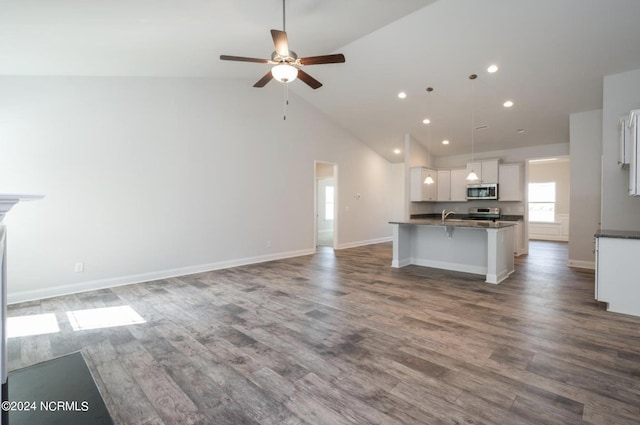 kitchen with open floor plan, appliances with stainless steel finishes, dark countertops, and dark wood-style floors