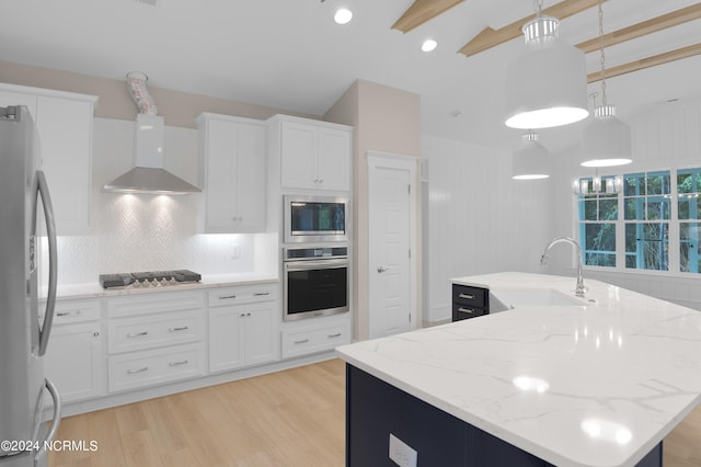 kitchen featuring hanging light fixtures, appliances with stainless steel finishes, a center island with sink, wall chimney exhaust hood, and tasteful backsplash