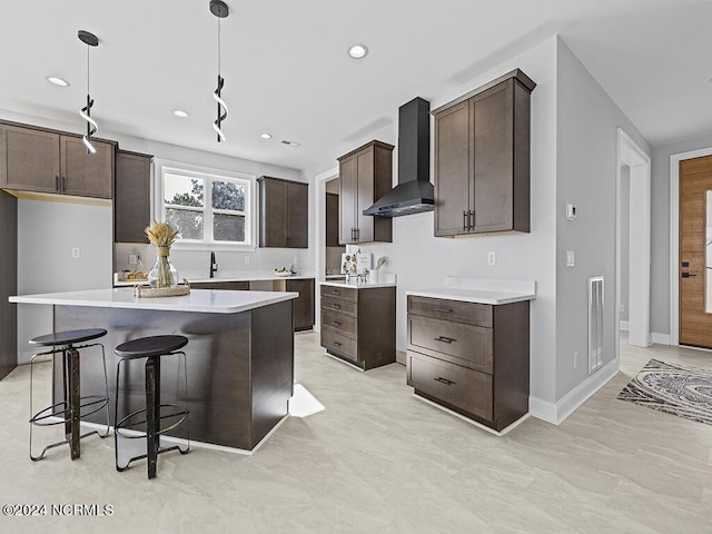 kitchen with pendant lighting, light countertops, a kitchen island, wall chimney range hood, and dark brown cabinetry