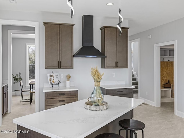 kitchen featuring baseboards, a center island, wall chimney range hood, a kitchen bar, and recessed lighting