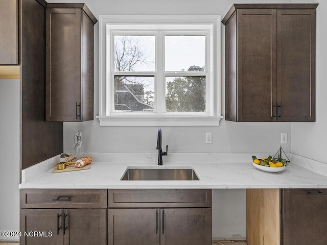 kitchen featuring dark brown cabinetry, light stone counters, and a sink