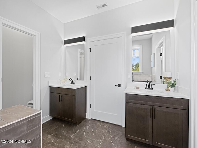 bathroom featuring marble finish floor, two vanities, visible vents, toilet, and a sink