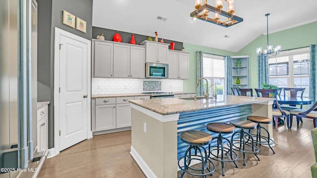kitchen featuring light wood-style floors, a sink, a notable chandelier, vaulted ceiling, and stainless steel appliances