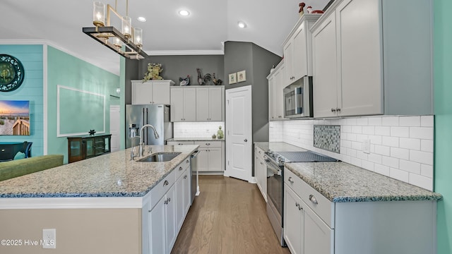 kitchen featuring a kitchen island with sink, appliances with stainless steel finishes, wood finished floors, a sink, and light stone counters