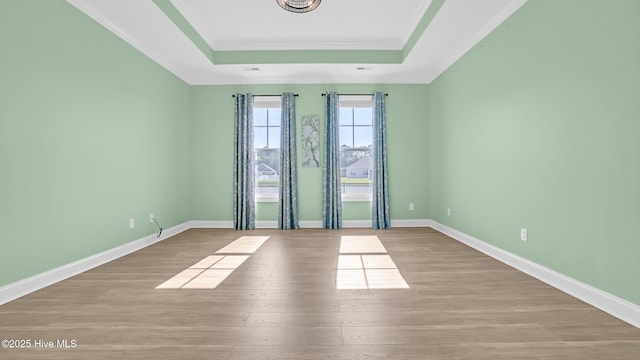 empty room with baseboards, a tray ceiling, crown molding, and wood finished floors