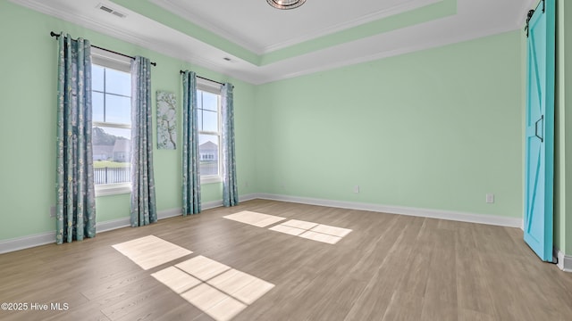 spare room with visible vents, ornamental molding, baseboards, a raised ceiling, and light wood-style flooring