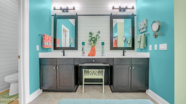 full bath with double vanity, tile patterned flooring, a sink, baseboards, and wooden walls