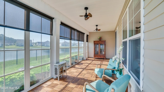 sunroom / solarium featuring a water view, a ceiling fan, wood walls, and a wood stove
