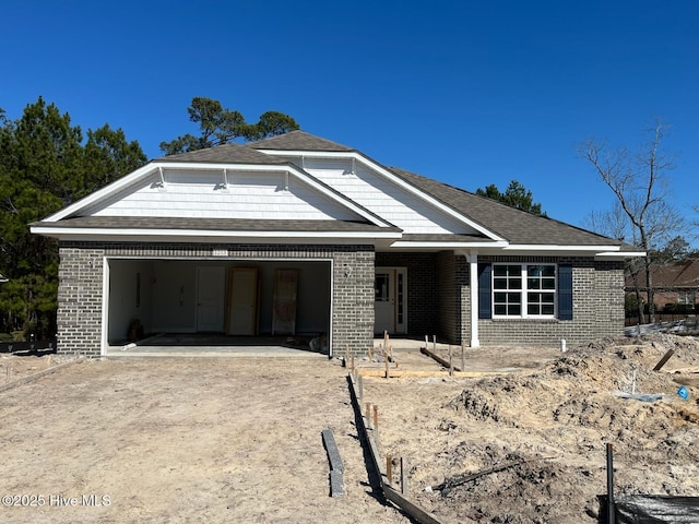 view of front of property featuring brick siding, driveway, an attached garage, and roof with shingles