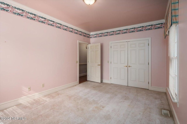 unfurnished bedroom featuring a closet, light colored carpet, and ornamental molding