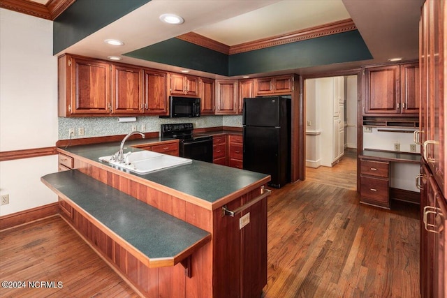 kitchen with sink, a tray ceiling, a breakfast bar, black appliances, and ornamental molding